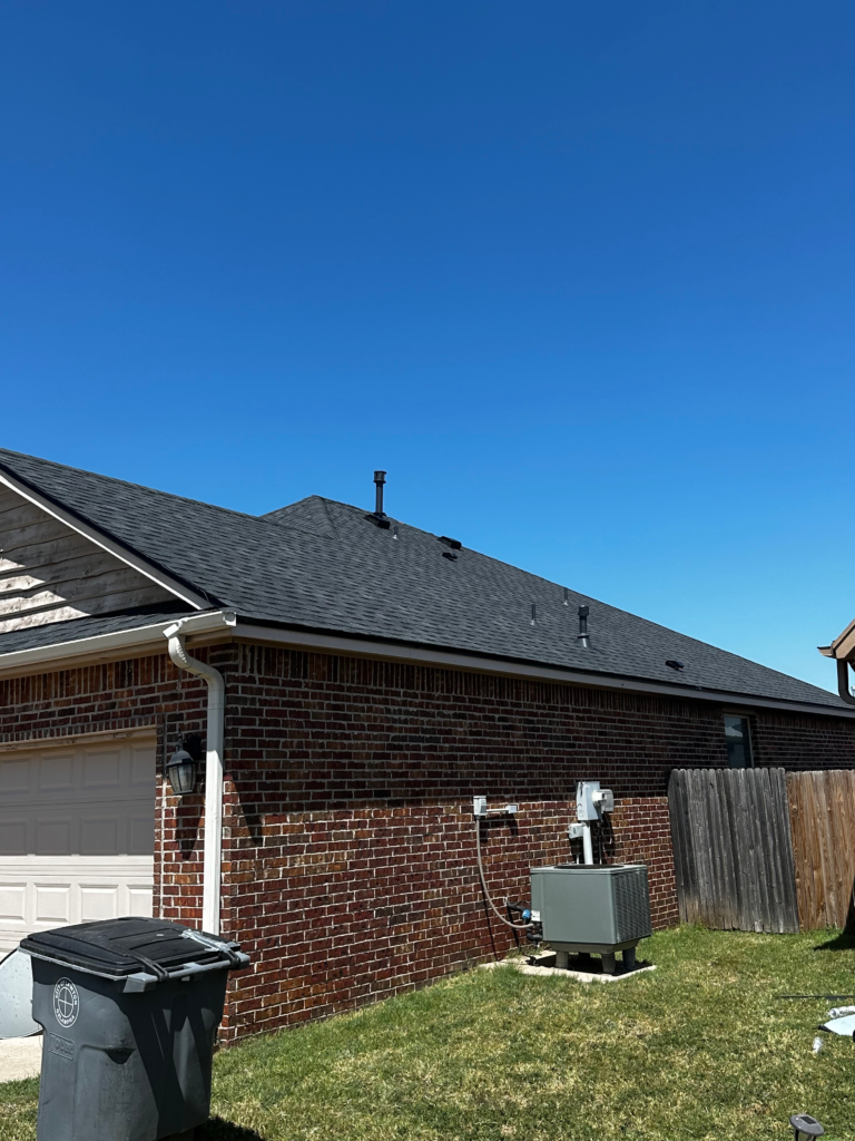 Close-up of newly installed dark gray asphalt shingles on Oklahoma home roof against blue sky