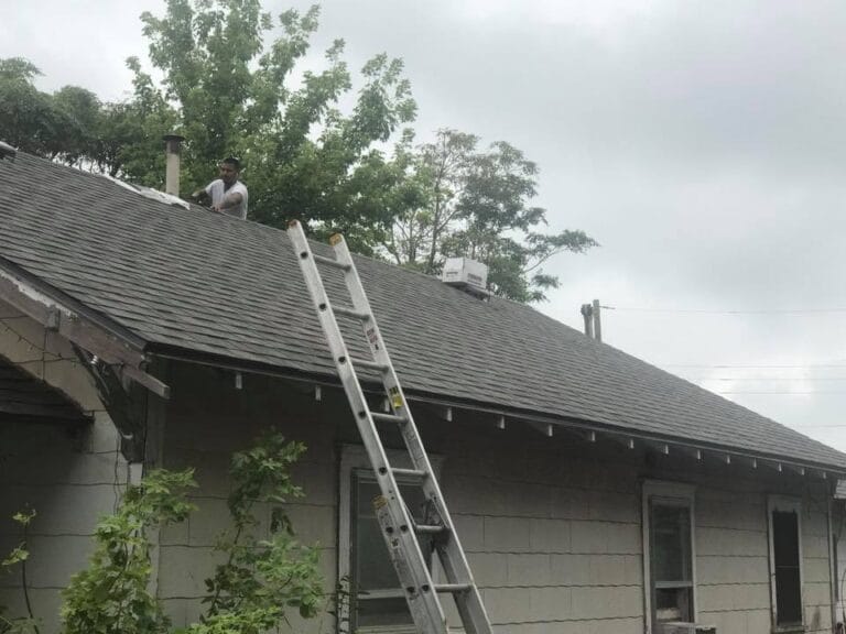 Oklahoma Roofing Experts crew member installing asphalt shingles on residential roof with ladder